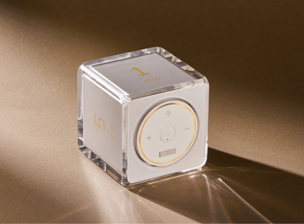 The clear acrylic Settledy cube with its light ring illuminated against a warm brown background