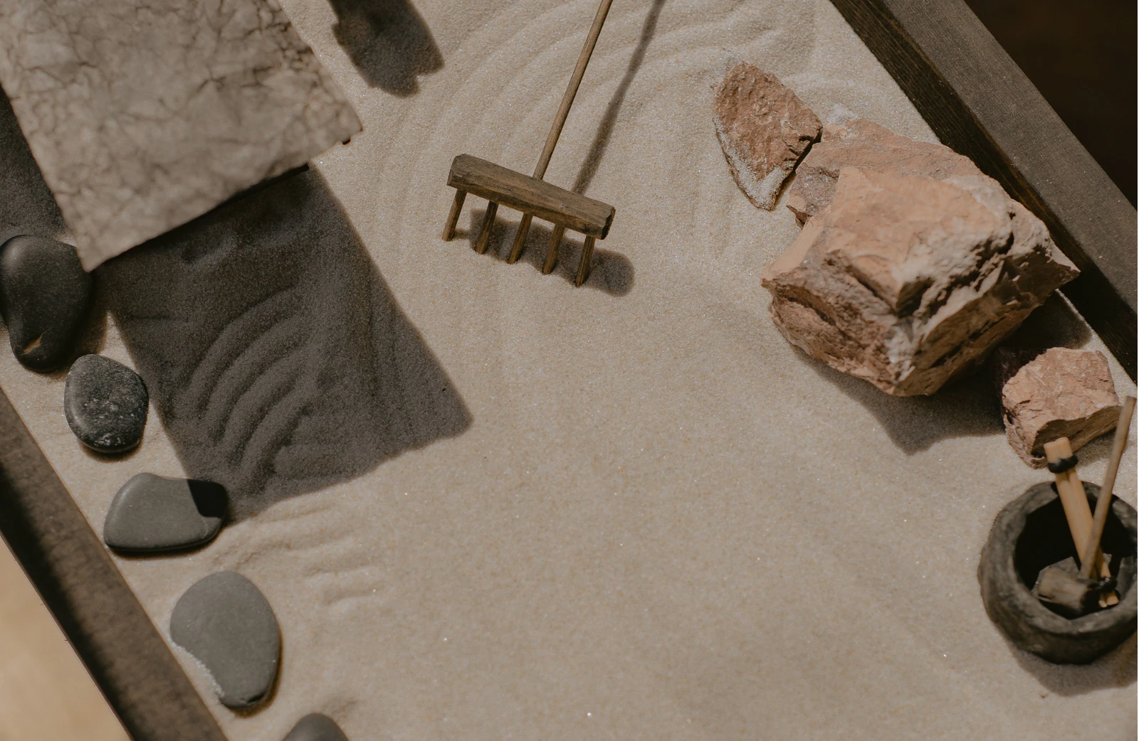 A miniature Zen garden with raked sand, stones, and a wooden rake